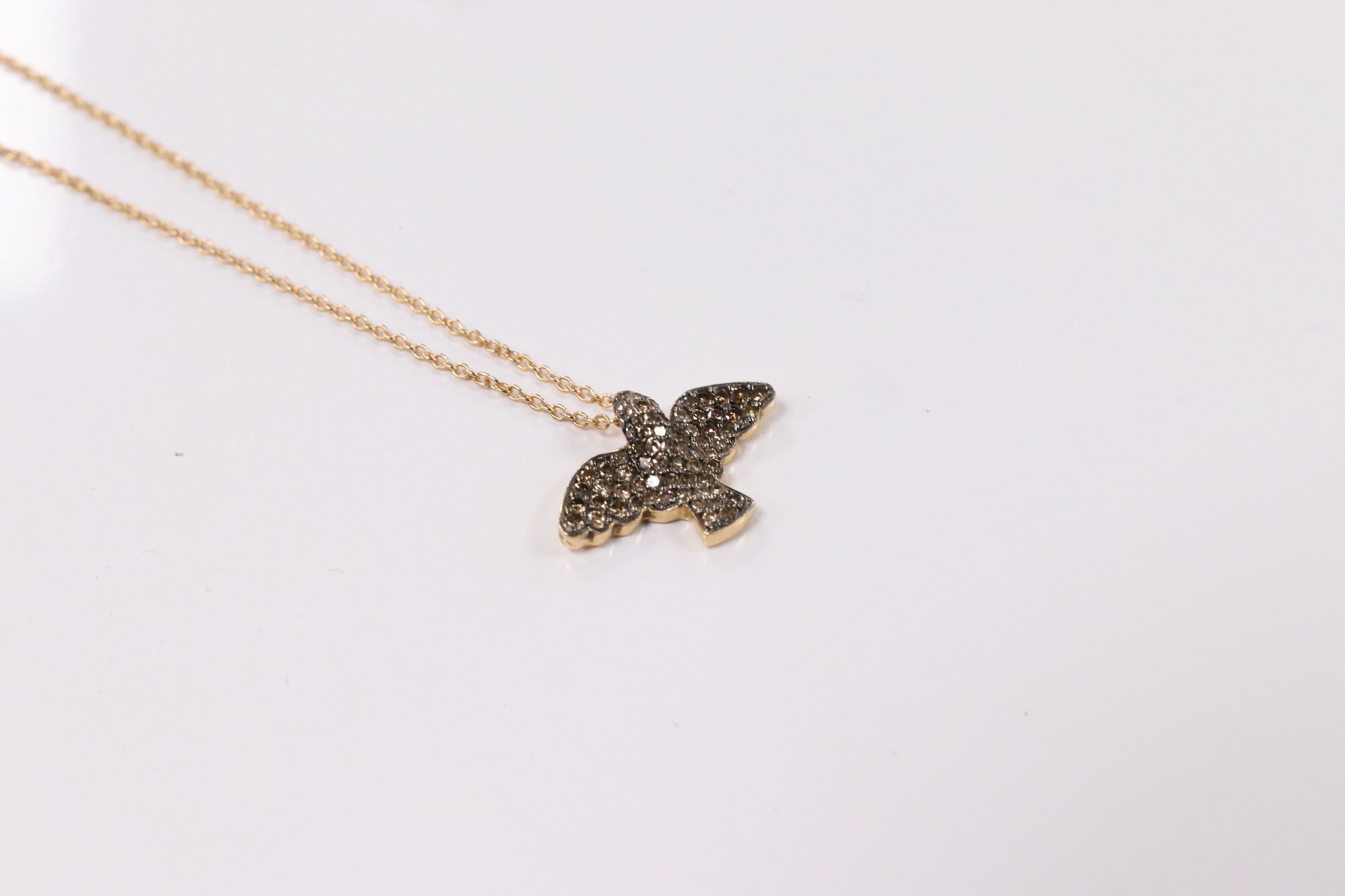 A modern 18k and pave set two colour diamond chip bird pendant, wing span 19mm, on an Italian 18k fine link chain, 36cm, gross weight 4.4 grams. Condition - fair to good